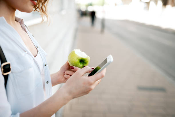 Using smartphone and eating apple in the city. Close-up.