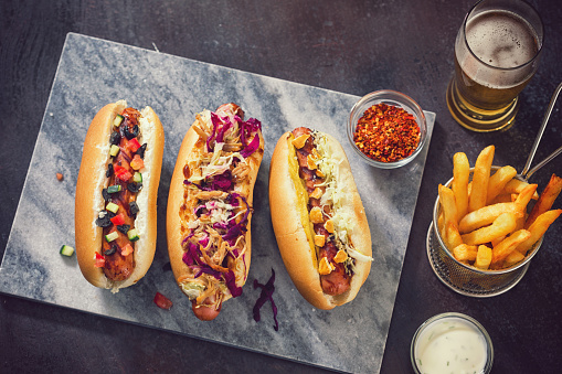 High angle view of freshly grilled  hot dogs with various condiments like barbecue sauce,pulled pork,coleslaw,sauerkraut,pretzels,tzatziki,cucumber and kalamata olives