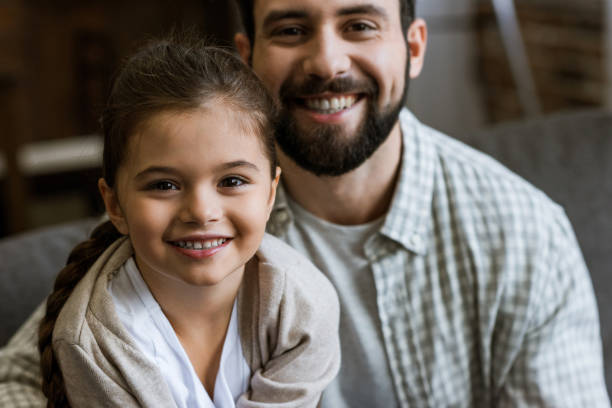 istock cheerful father and daughter hugging and looking at camera at home 956133372