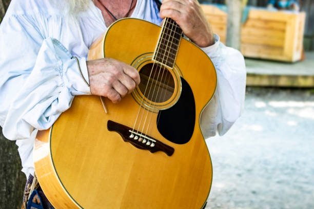 istock Guitar held by man in historical white peasant shirt with rustic stage blurred in background 956136844