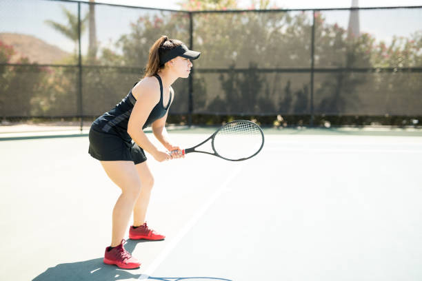 Professional female tennis player training on court Profile view of professional female tennis player standing on the base line ready to play baseline stock pictures, royalty-free photos & images