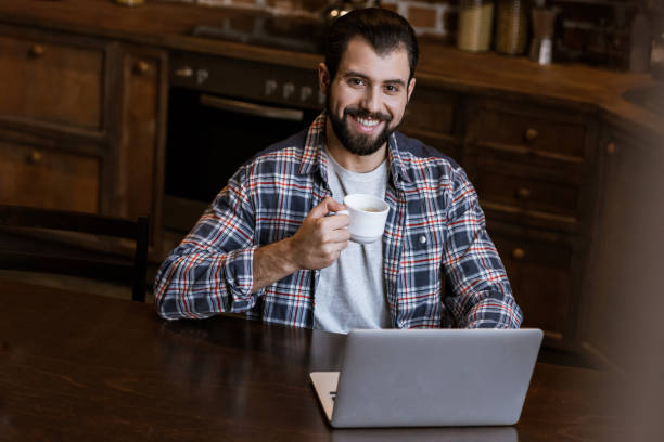 istock handsome man with coffee cup sitting at table with laptop 956140084