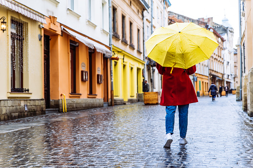 woman in red coat with yellow umbrella walk by street in rainy weather. copy space