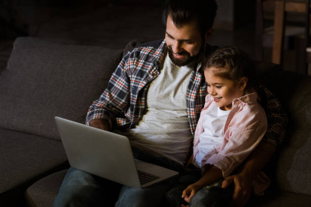 istock cheerful father with daughter sitting on couch and using laptop 956147620