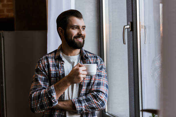 istock happy handsome man with coffee cup looking at window 956148356