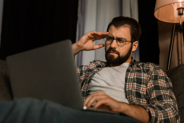 istock tired man in glasses sitting on couch with laptop 956151012