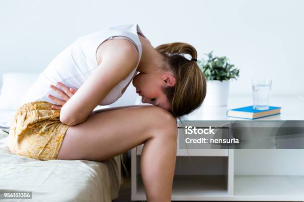 Unhealthy Young Woman With Stomachache Leaning On The Bed At Home Stock Photo - Download Image Now