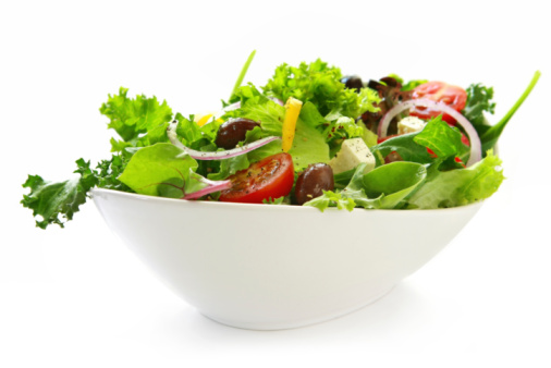 Delicious homemade gourmet healthy green salad bowl, with green salad lettuce, olive oil, garlic and fresh cherry tomatoes in olive oil, served in a  ceramic bowl, with seasoning and herbs on a natural wooden kitchen or restaurant table, representing a healthy lifestyle, wellbeing and body care, side view with a copy space