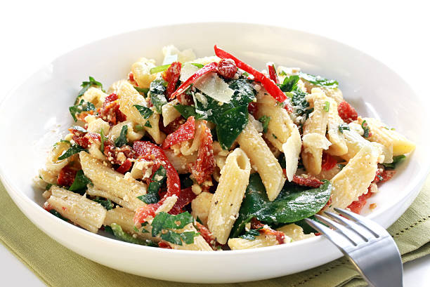 Close up of delicious pasta on white plate Pasta salad with spinach leaves, bell peppers, sundried tomatoes, and parmesan cheese.  Healthy fresh eating.  Please see also: spinach pasta stock pictures, royalty-free photos & images