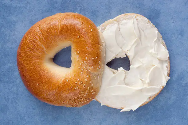 Cut bagel spread with cream cheese, over blue slate background.  More sandwiches: