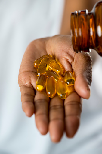 Close-up of a person's hands holding a bottle of omega 3 capsules.