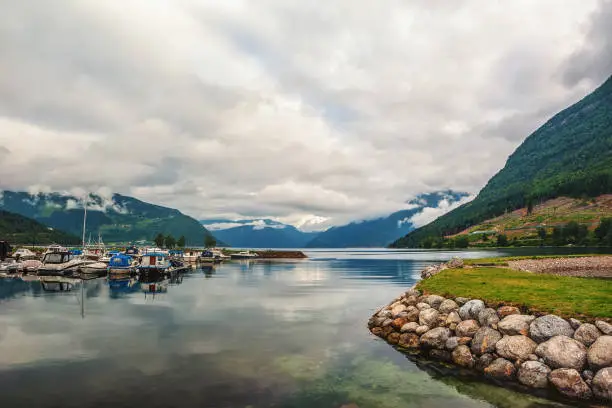 Photo of Beautiful view of the Parking of yachts and boats in the Bay of the Norwegian fjord. Mountain view in cloudy, dramatic weather.
