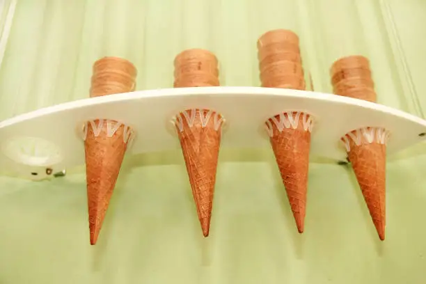 Ice cream waffle cones on dispenser. Ice cream cornets packed in dispenser on the wall of the store. Italian pastry-shop. Sweet, egg product, summer season. Shop of sweets, dessert.