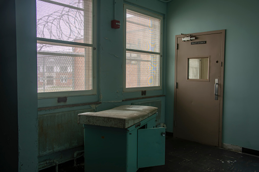 Dirty, rusting treatment table inside prison hospital with fence and razor wire through window.