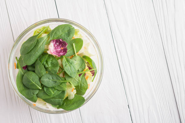 Fresh green salad with spinach, arugula, romaine and lettuce in bowl on white wooden background. Copy space