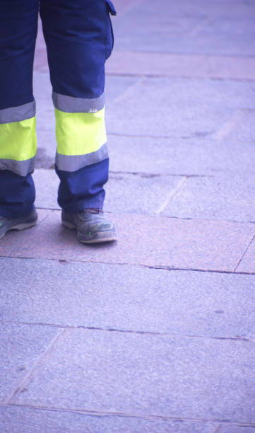 istock Municipal workers on sidewalk pavement standing in work uniform with hard toe boots and reflective strips.. 956189184