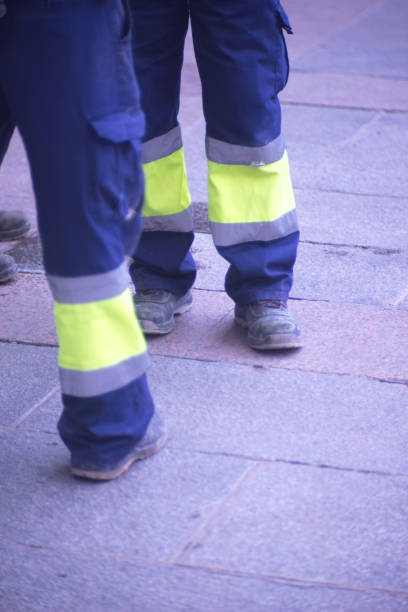 istock Municipal workers on sidewalk pavement standing in work uniform with hard toe boots and reflective strips.. 956189190