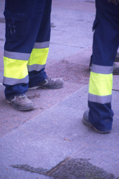 istock Municipal workers on sidewalk pavement standing in work uniform with hard toe boots and reflective strips.. 956189192