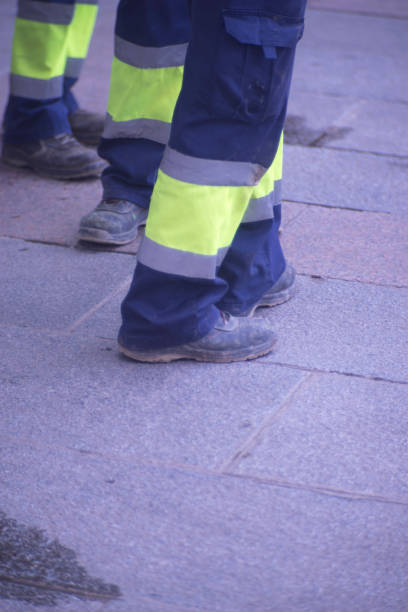 istock Municipal workers on sidewalk pavement standing in work uniform with hard toe boots and reflective strips.. 956189196
