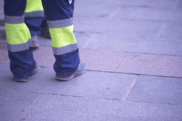 istock Municipal workers on sidewalk pavement standing in work uniform with hard toe boots and reflective strips.. 956189198