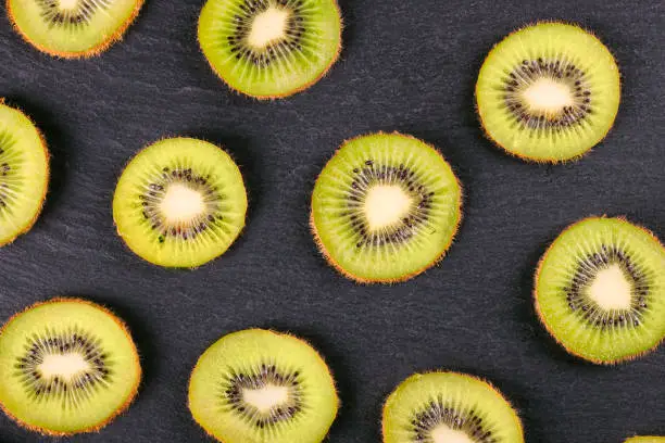 Photo of kiwi fruit slices on black slate background.