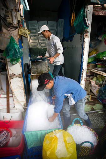 Ho Chi Minh City, Vietnam - January 23, 2018: Vietnamese men grinding and crushing ice for sale at Ben Thanh Market in Ho Chi Minh City, Vietnam.