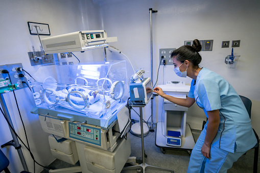 Neonatal nurse checking baby's monitor while newborn is treated for jaundice in incubator at the hospital