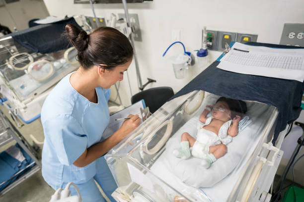 istock Beautiful premature baby in an incubator sleeping and nurse checking him while taking notes on a clipboard 956193158