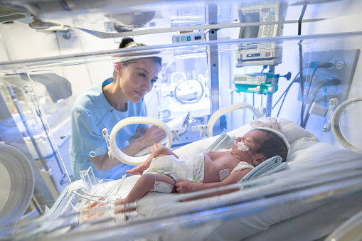 Beautiful sweet nurse checking a premature baby in the neonatal intensive care unit taking notes on a clipboard