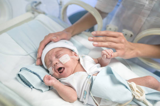 sweet premature baby in an incubator and unrecognizable mom caressing baby trying to calm him down - new childbirth new life love imagens e fotografias de stock