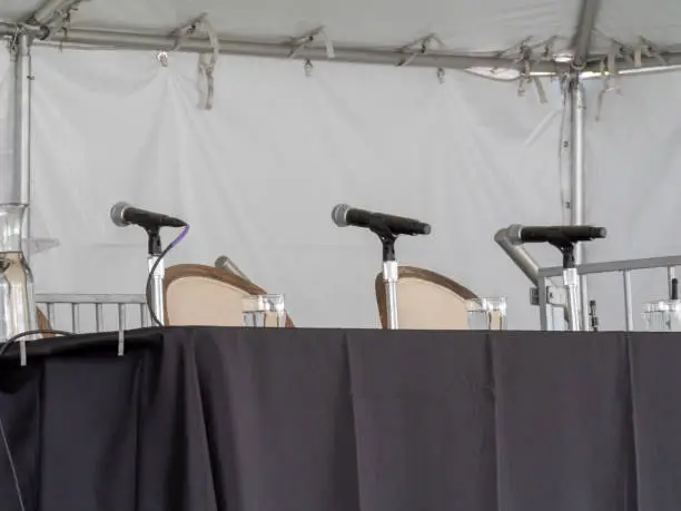 Row of three microphones sitting on table, awaiting speakers