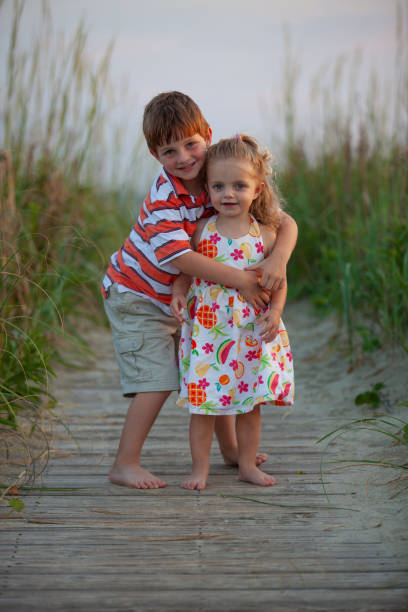Portrait. Brother and sister as children hug on the beach at sunset.  bald head island stock pictures, royalty-free photos & images