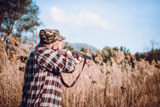 istock Male Hunter Hidden in the Swamp and Preparing for Shooting 956211052
