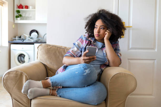 istock Pensive young woman using smart phone at home 956218246
