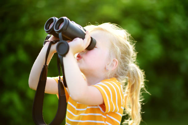 istock Funny little girl looking through binoculars on sunny summer day 956221818