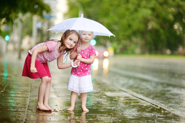 dos lindas hermanitas divirtiéndose bajo una lluvia - child dancing preschooler outdoors fotografías e imágenes de stock