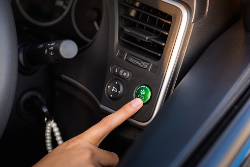 Close-up portrait of woman finger pressing switch on/off of eco mode in the car.