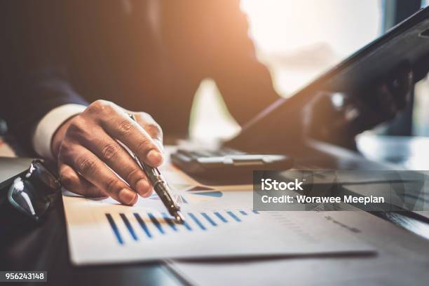 Close Up Businessman Consultant Holding Pen And Pointing At Financial On Wooden Desk In Coffee Shop Freelance Tax Accounting Statistics And Analytic Research Concept Stock Photo - Download Image Now