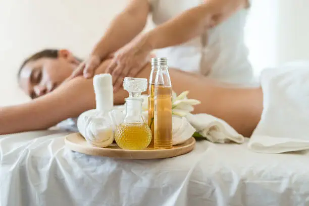 Bottle of essential oil on a wooden tray. background Young beautiful Asian woman relaxing in the spa massage