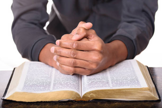 istock Hands of a young man folded praying over a Bible, hands over soft focus Bible 956273406