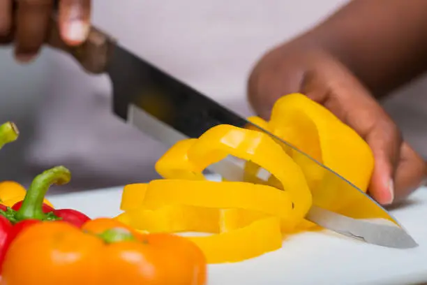 Hands cutting bell peppers with knife, food preparation, cuisine and cooking concept