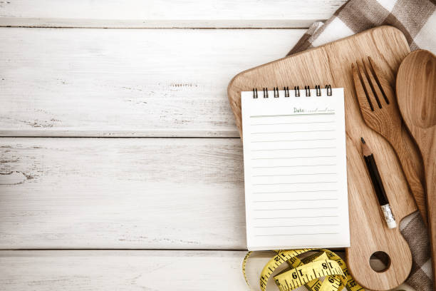 istock Notepad on chopping board with wooden fork and spoon  on white table , recipes food or diet plan for the healthy habits shot note background concept 956291336