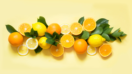 Summer set of tropical fruits, lemon, orange and green leaves on yellow. Banner. Top view.