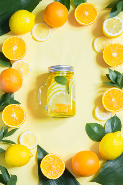 Summer fruits water with lemon, orange, mint and ice in mason jar on yellow. Tropical concept. Summer fruits water with lemon, orange, mint and ice in mason jar on yellow. Tropical concept. Top view. mason jar lemonade stock pictures, royalty-free photos & images