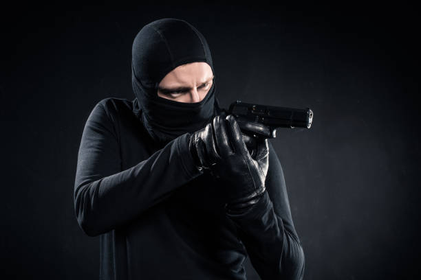istock Burglar in balaclava aiming with gun on black 956306010