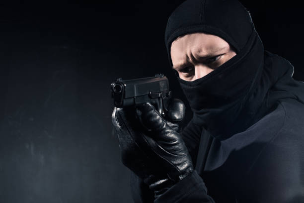istock Robber in balaclava and gloves aiming with gun on black 956306180