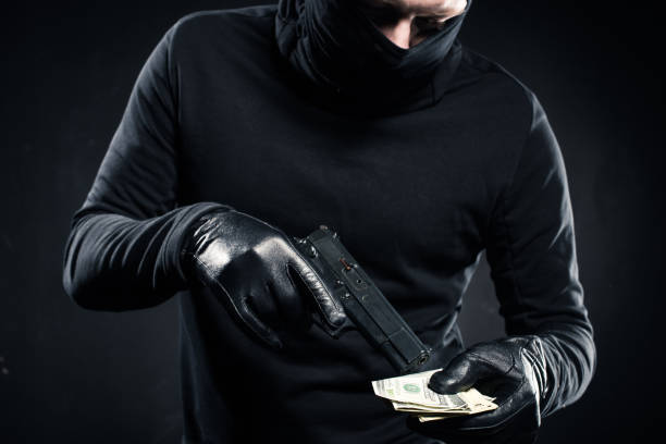 istock Man in black balaclava holding gun and dollars 956306262
