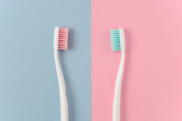 nahaufnahme von zwei kunststoff weiß zahnbürsten mit rosa und blauen borsten auf rosa und blauen hintergrund. kostenloses exemplar raum. - toothbrush pink turquoise blue stock-fotos und bilder