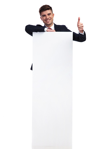 laughing businessman with message on board makes ok sign while standing on white background behind the board, full body picture