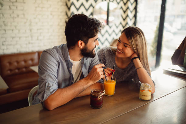 Happy couple is drinking juice with two straws in cafe